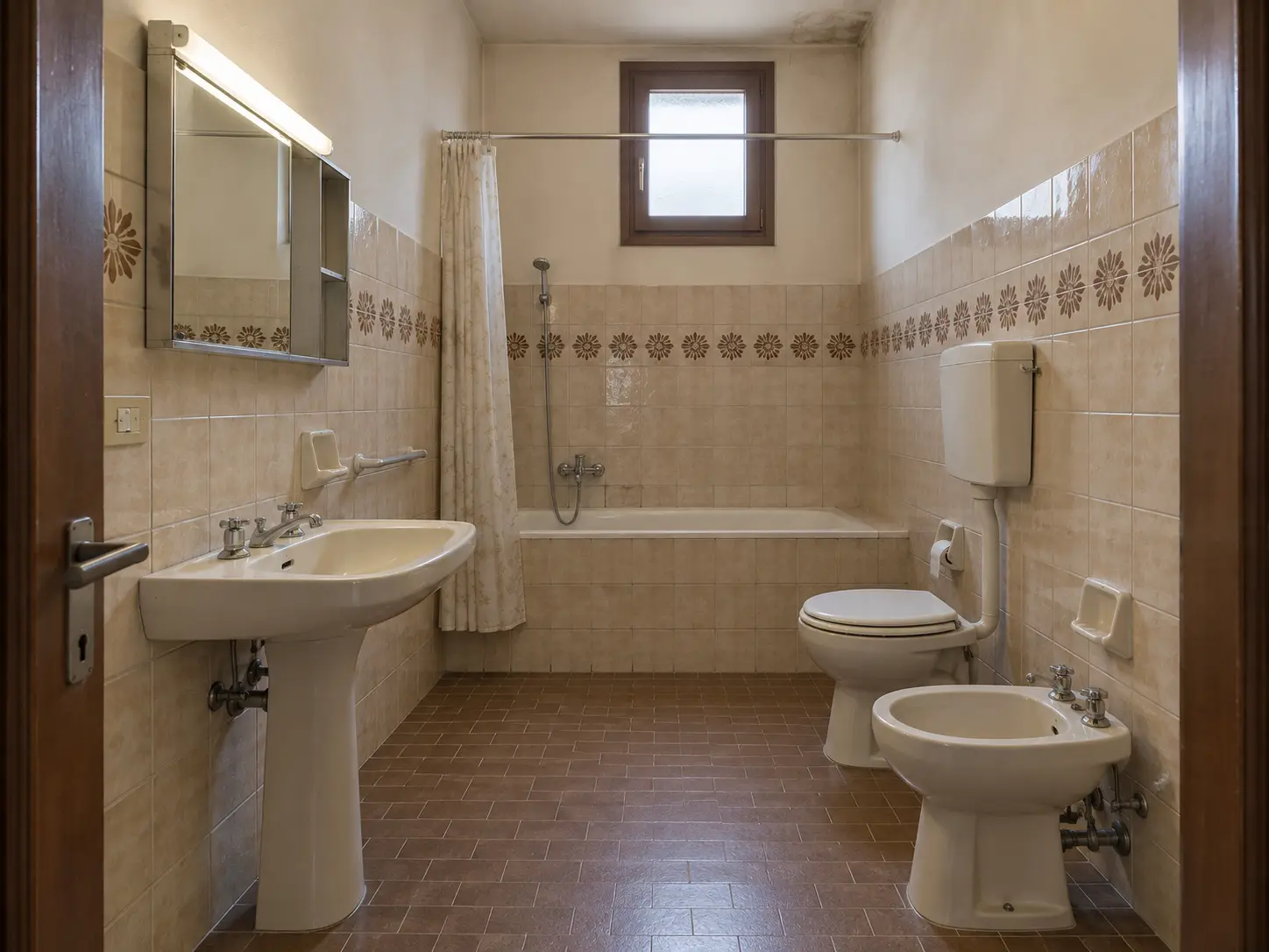 Il bagno prima dei lavori: vasca in muratura, piastrelle beige con greca a fiori, sanitari a pavimento